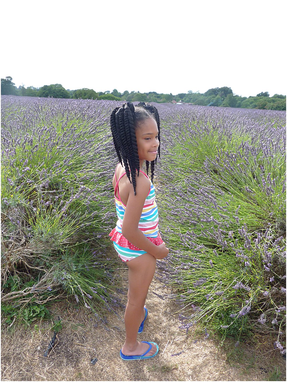 Little black girl in a lavender field wearing key trend for the SS18 season rainbow stripe swim suit.